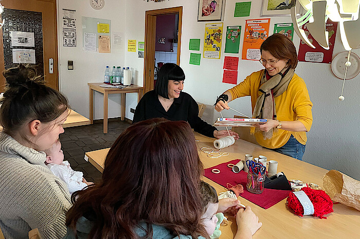 Mütter mit Kindern und Mitarbeiterinnen sitzen in der Wohngruppe am Tisch.