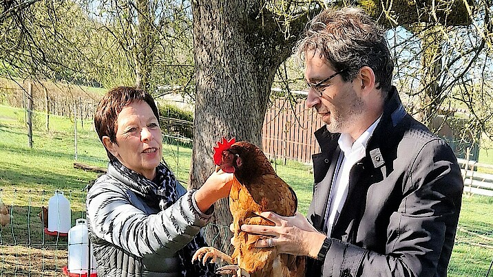 Staatssekretär Dr. André Baumann und Margret Frank vom Ministerium für Umwelt, Klima und Energiewirtschaft nehmen ein Huhn auf den Arm.