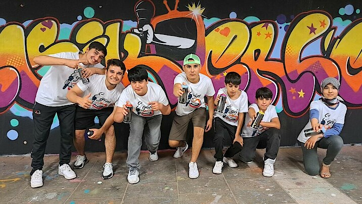 Bild zeigt die Teilnehmer auf einem Gruppenbild vor einem bunten Graffiti