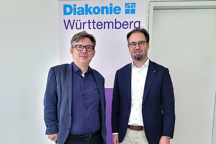 Knapp und Rosemann stehen vor einem Aufsteller mit Diakonie-Logo.