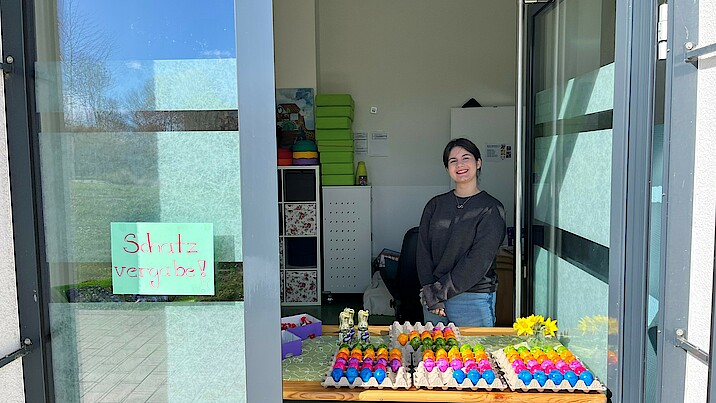Bild zeigt ein junges Mädchen die hinter einem Stand mit vielen bunten Eiern steht