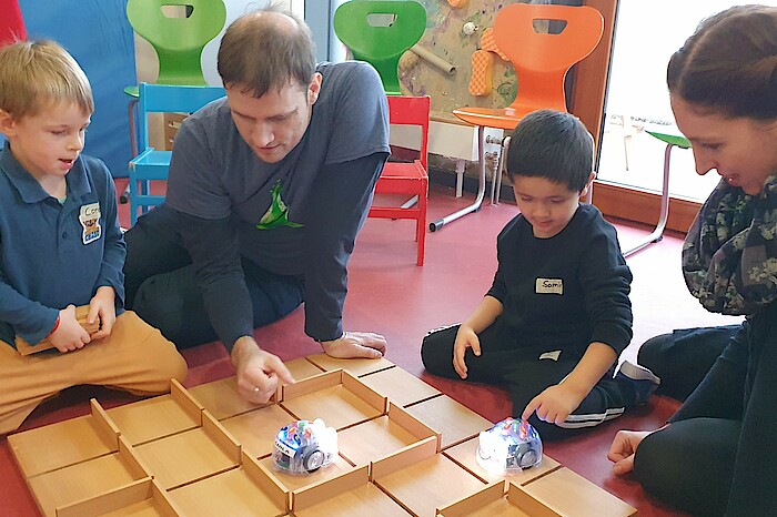 Mitarbeitende und zwei Kinder sitzen mit den Minirobotern auf dem Boden.