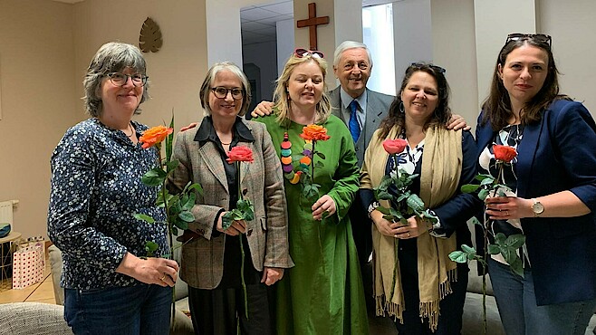 Vier Frauen mit Rosen in der Hand und ein Mann stehen in einer Kirche und lachen in die Kamera.